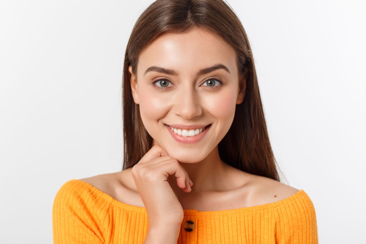 Young woman smiling at camera wearing yellow shirt against white background
