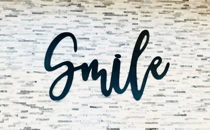 Black cursive "Smile" text on white brick wall background for orthodontics practice