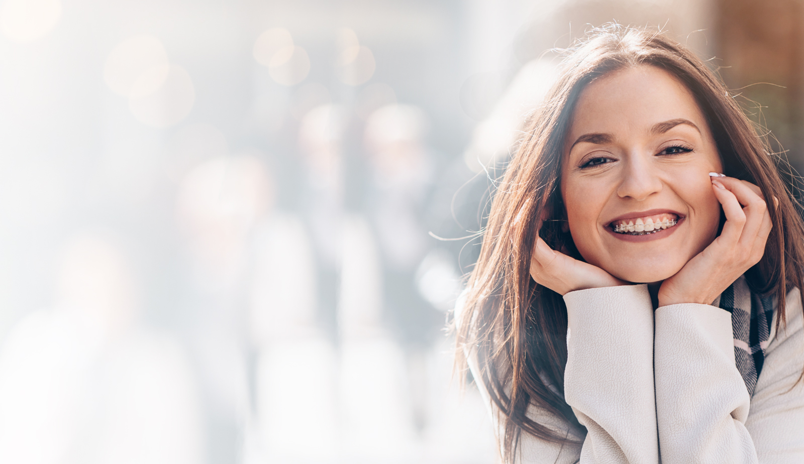 Woman smiling outdoors in winter clothing with snowy background, orthodontics patient portrait.