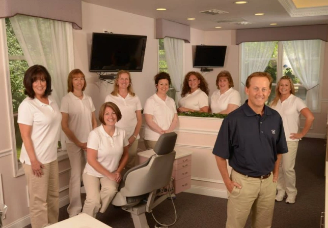 Dr. LaPonzina's orthodontic team poses together in modern office reception area wearing matching uniforms.