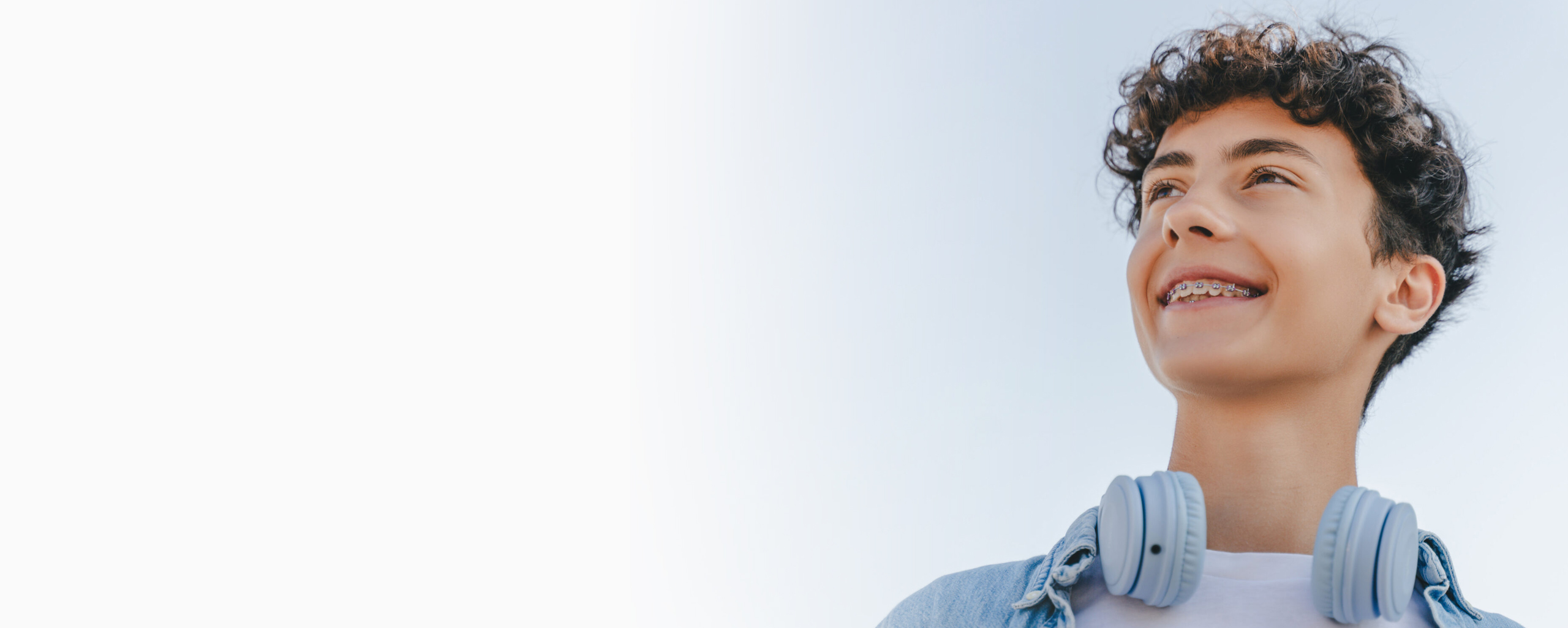 Young man looking upward thoughtfully wearing casual blue shirt against light background.