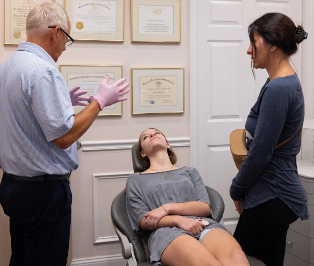 Orthodontist consulting with patient and staff member in modern office with diplomas on wall.