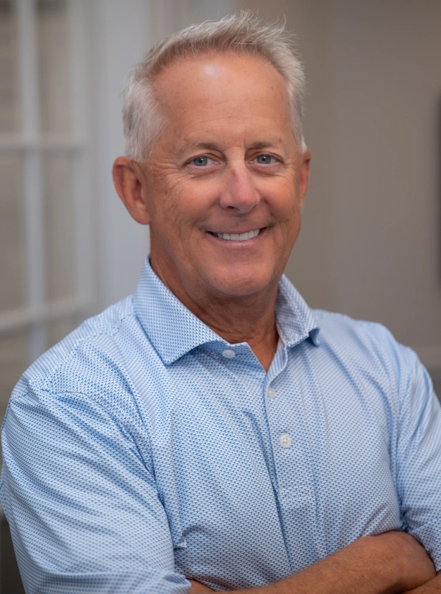 Professional headshot of smiling man in light blue shirt against neutral background