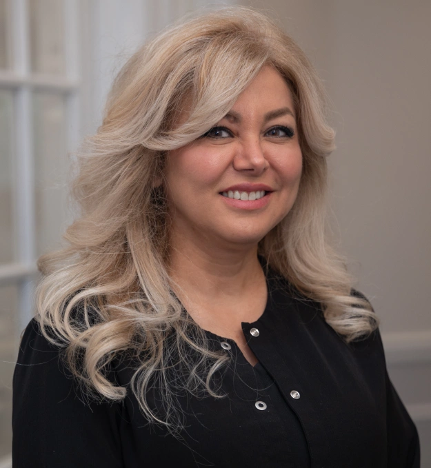 Professional woman with blonde wavy hair smiling in black blazer against neutral background.