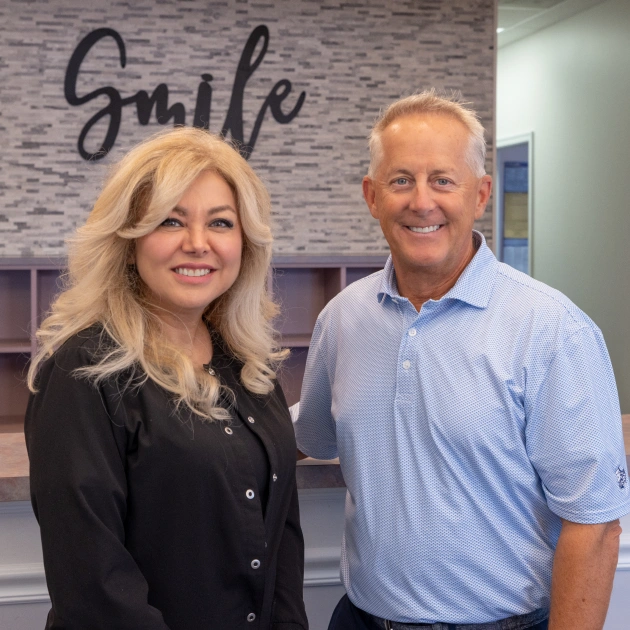 Two professionals posing together in modern orthodontic office with "Smile" signage visible.