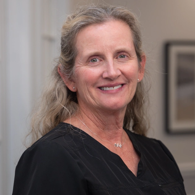 Professional woman in black scrubs smiling at camera in medical office setting.