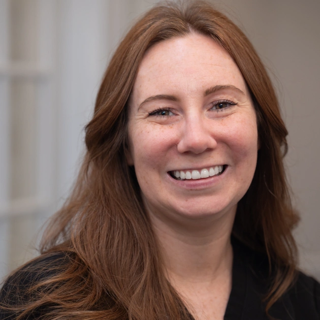 Woman with long brown hair smiling at camera in professional indoor setting