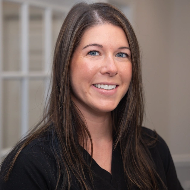 Professional headshot of woman smiling at camera in clinical office setting.