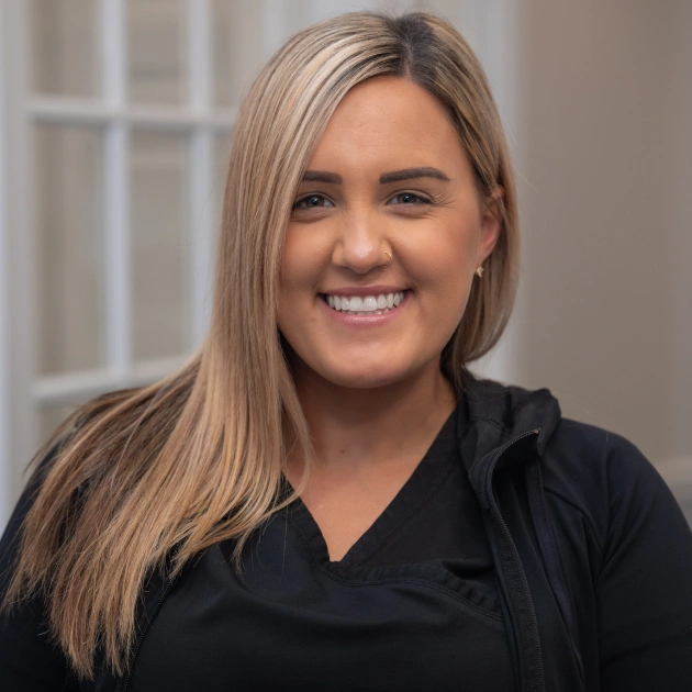 Professional woman smiling at camera in black shirt, indoor office setting.