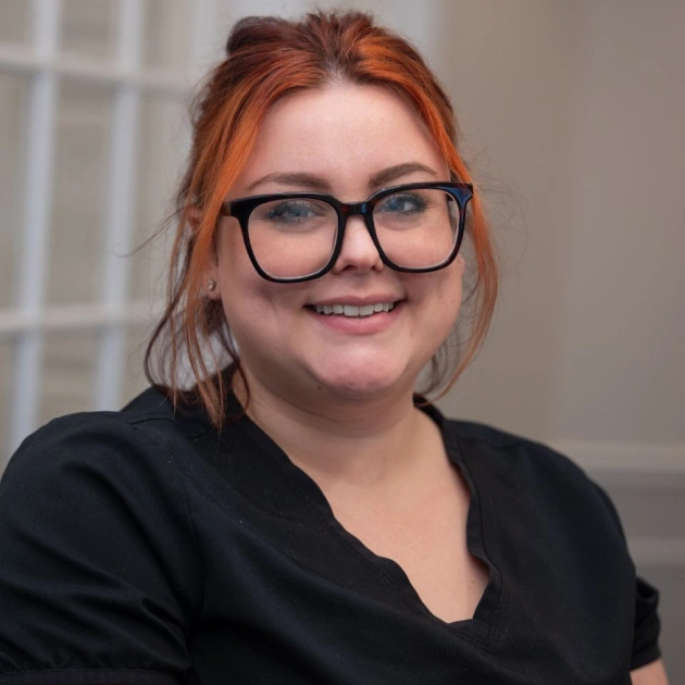 Woman with red hair and glasses smiling at camera in professional office setting.