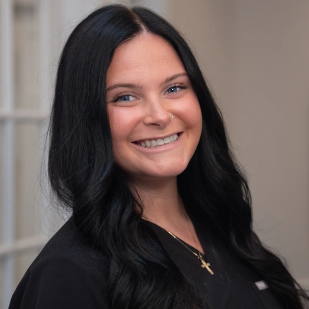 Smiling woman with long black hair wearing black top in professional office setting.
